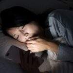 2026 擺脫熬夜拖延實測：在深夜漆黑的臥室中，一位夜貓子躺在床上被手機螢幕藍光照亮面部，展現現代人因白天壓力引發深夜報復性分心與睡眠拖延的真實生活痛點場景。